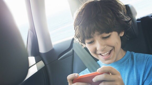 Kind spielt mit Smartphone im Auto