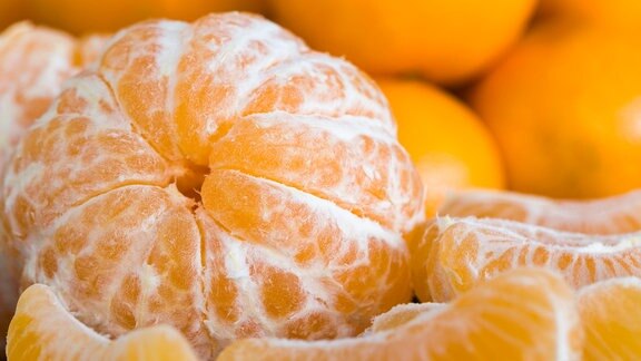Nahaufnahme von Clementinen, helleres Fruchtfleisch, im Hintergrund unscharf ungeschälte Früchte.
