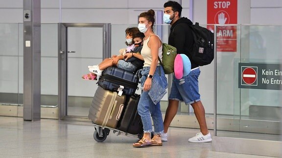 Eine Familie mit ihren Koffern am Flughafen München. Alle tragen Mundschutz.
