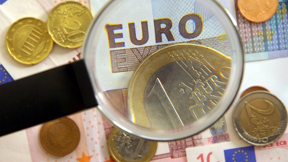 Euroscheine und Münzen werden mit Lupe geprüft.