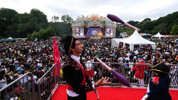 Ein Gaukler jongliert auf dem Tomorrowland Electronic Music Festival in Porto, 07/27/2019. Im Hintergrund ist eine Bühne des Festivals mit Besuchern davor zu sehen.