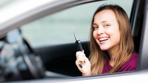 Eine junge Frau sitzt in einem Auto und zeigt den Autoschlüssel