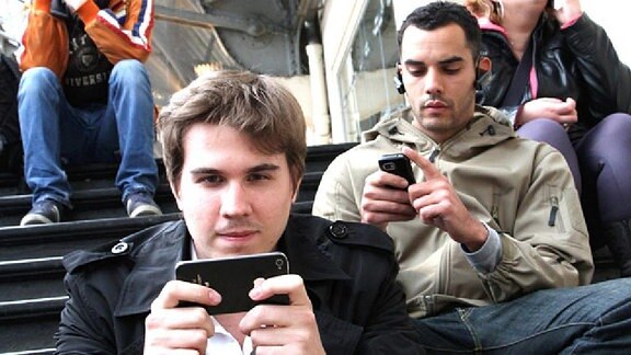 Junge Leute mit Smartphones sitzen auf einer Treppe.