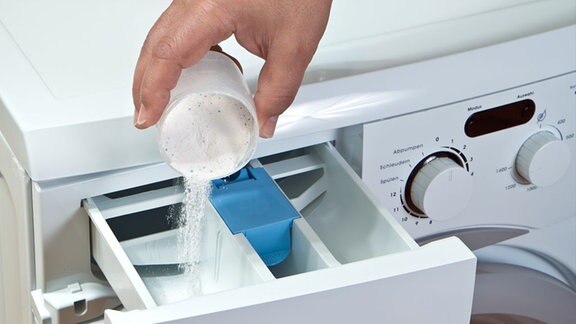Eine Hand füllt Waschmittel in eine Waschmaschine
